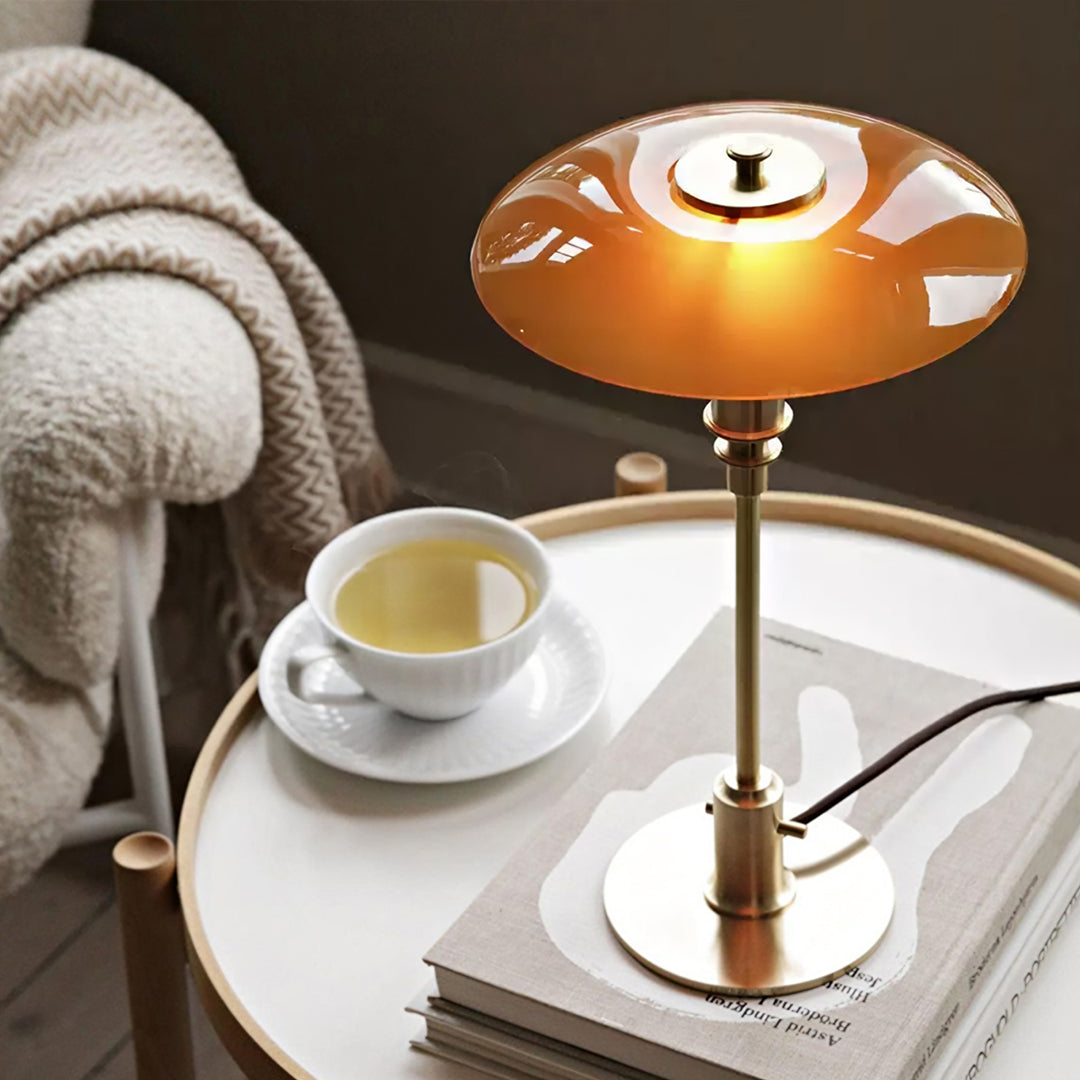 Table lamp with a warm glow on a table next to a cup of tea and a book.  | Extraordinary Emporium UK