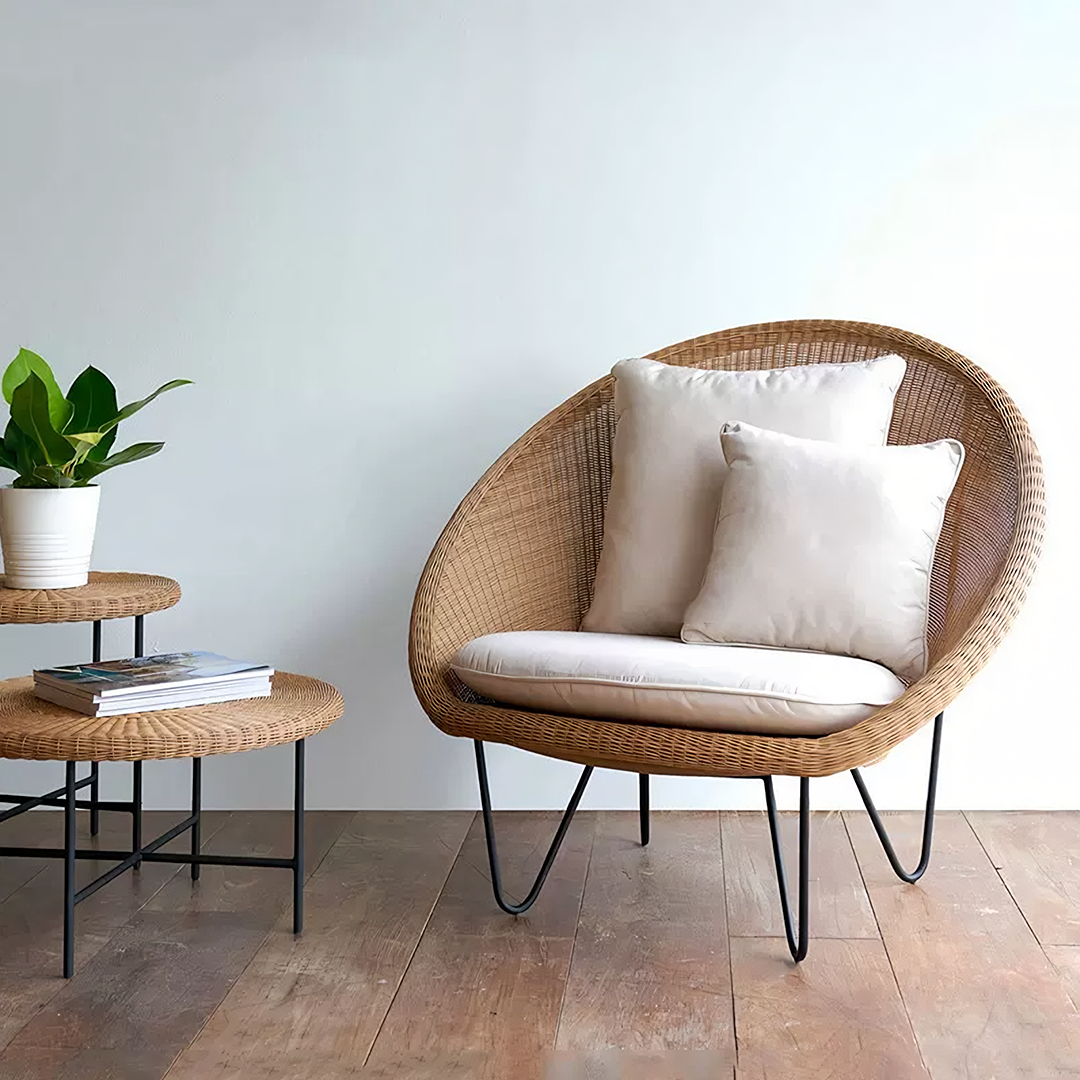 Wicker chair with cushions and a small table with a plant and books in a room.  | Extraordinary Emporium UK