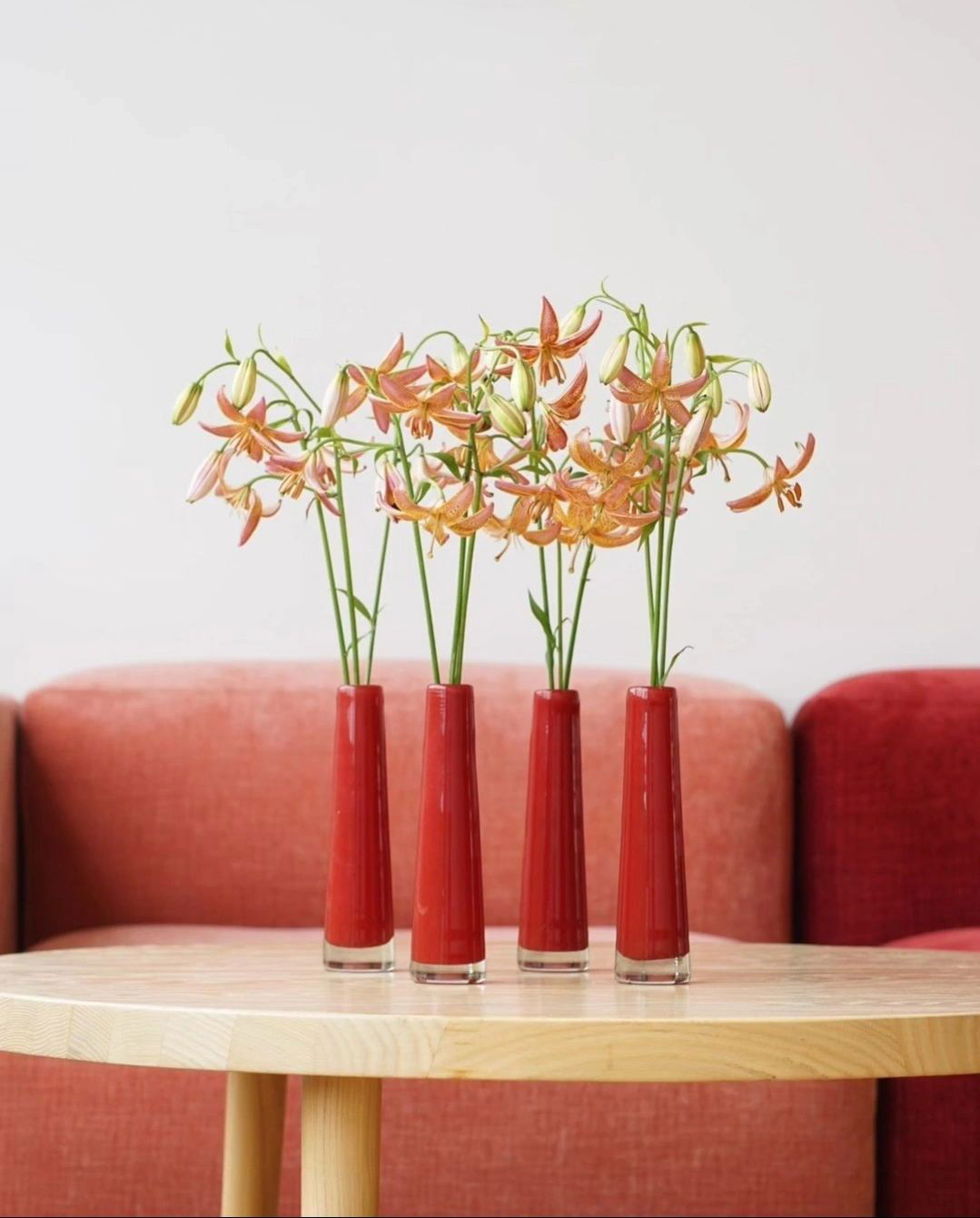 Four red vases with flowers on a wooden table against a red sofa. | Extraordinary Emporium 
