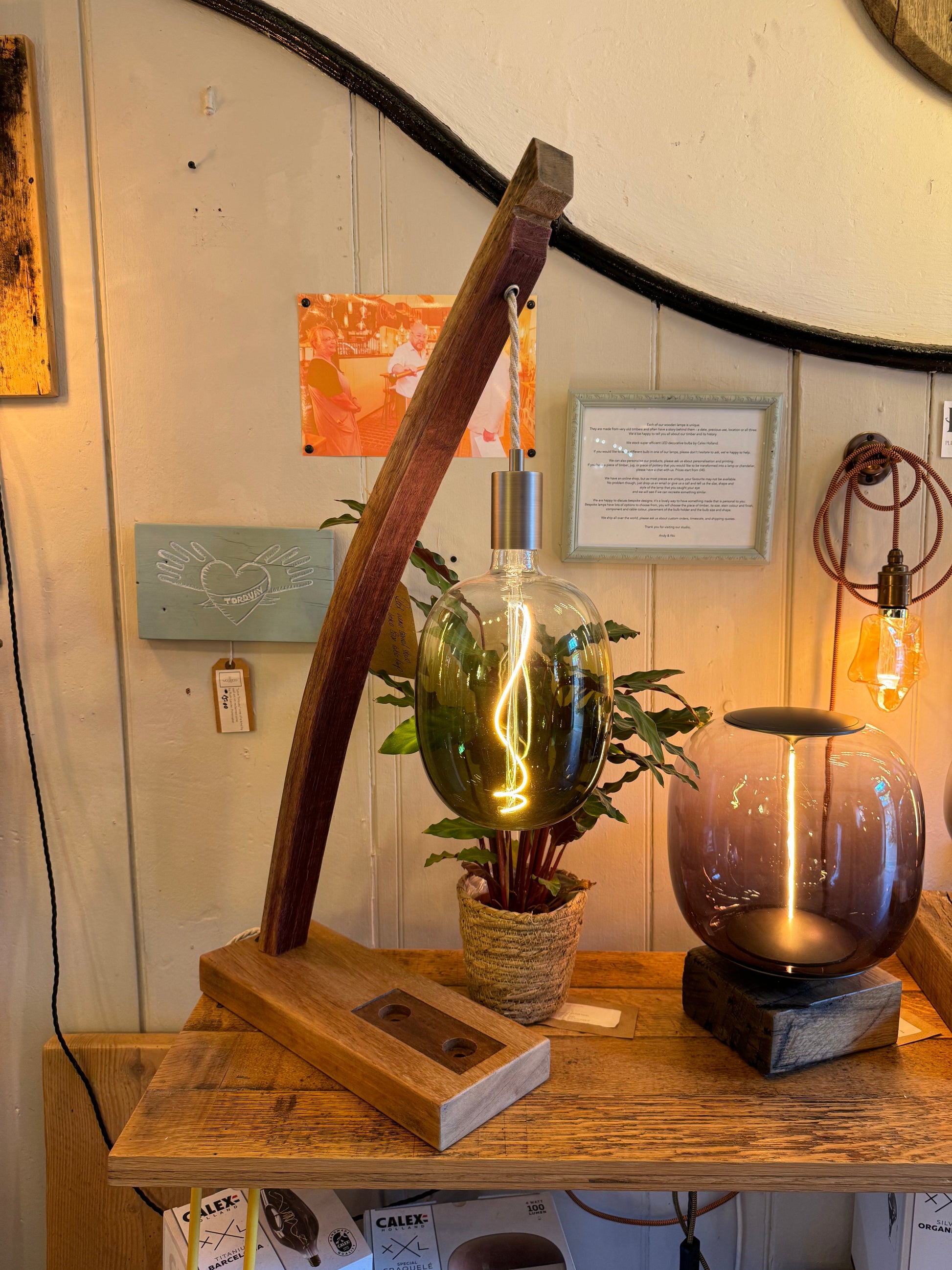 Decorative setup with a wooden stand, potted plant, and glass lamp on a wooden surface. | Extraordinary Emporium 