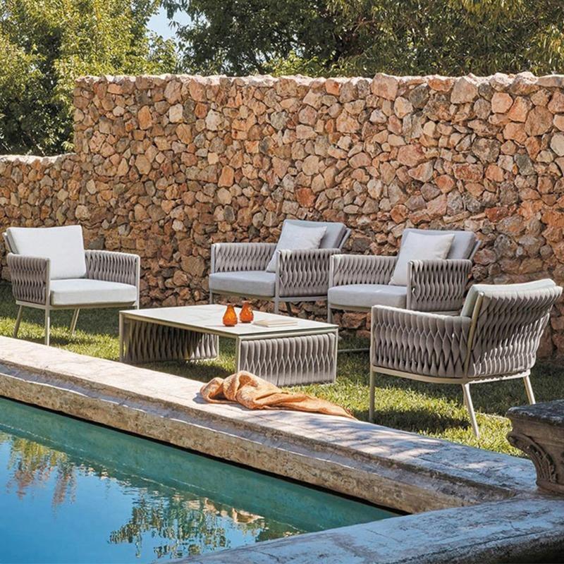 Outdoor patio furniture by a pool with a stone wall in the background | Extraordinary Emporium 