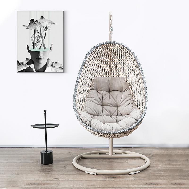 Hanging egg chair with cushion in a room with a side table and wall art. 