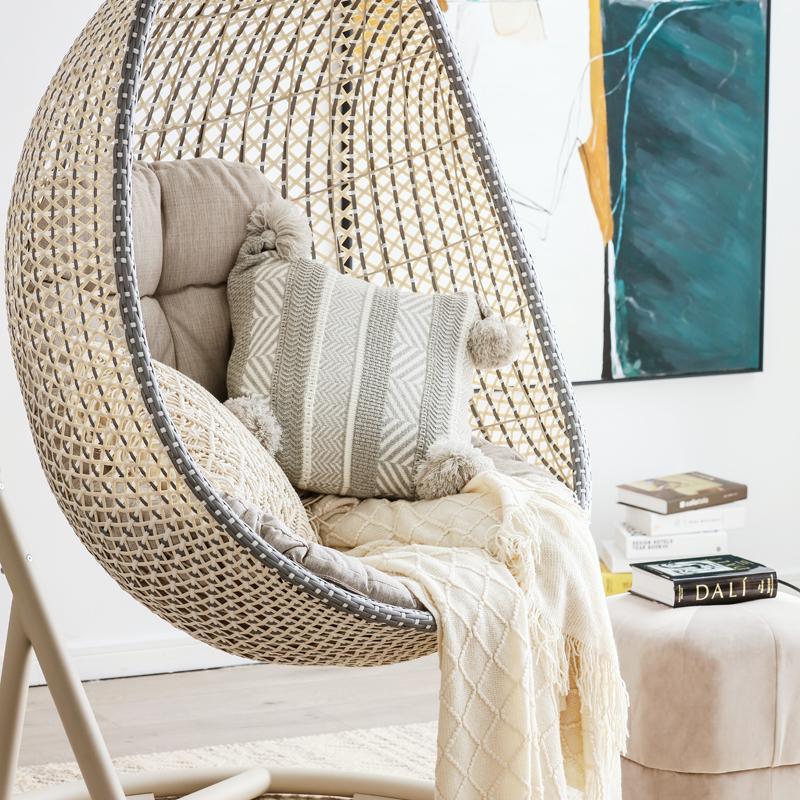 Woven egg chair with cushions and a blanket in a cozy room setting. | Extraordinary Emporium UK